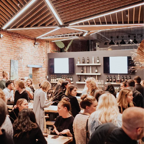 An event space with bright decorative lighting is filled with patrons holding glasses of wine