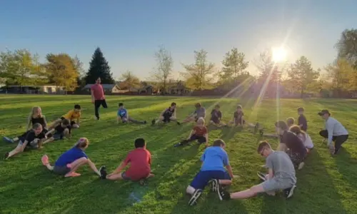 A group of young runners stretch in a circle on the grass